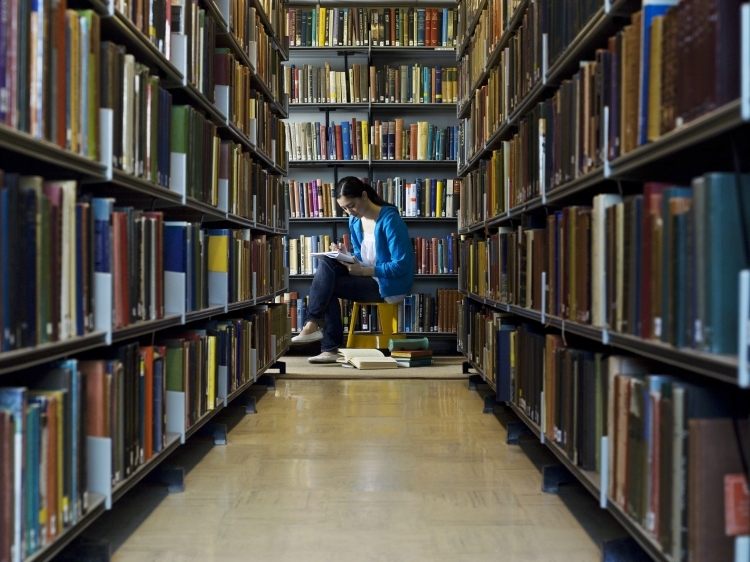 Gang met boekenrekken in een bibliotheek, een vrouw leest een boek