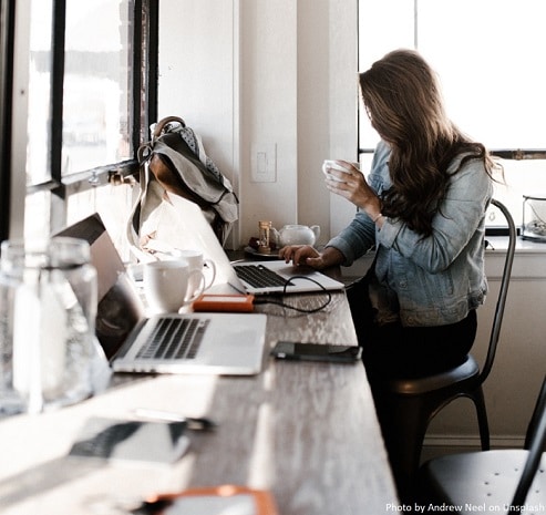 Attractieve vrouw die achter een modern en rommelig bureau zit met een kop koffie en een apple laptop
